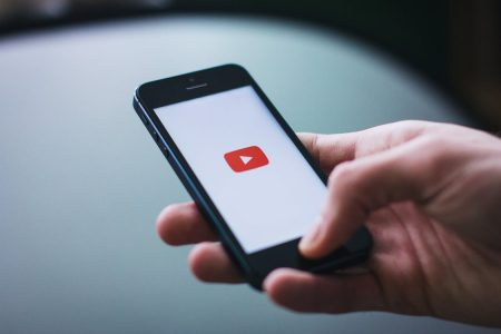 Person holding cellphone with the YouTube logo on the screen