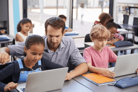 Teacher with students, looking at a computer. 3 Things IT Needs to Know About EdTech Collaboration with Teachers