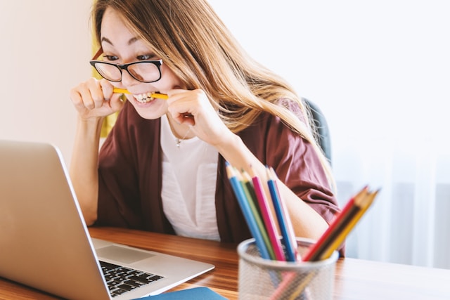 Female teacher gnawing on a pencil in frustration in front of a notebook computer.