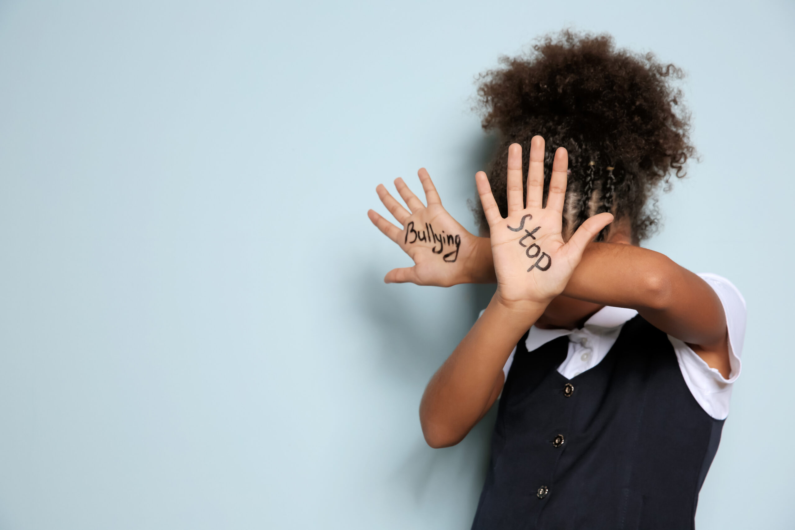 Little girl holding palms up to defend herself, the words 'stop' and 'bullying' written on her palms.