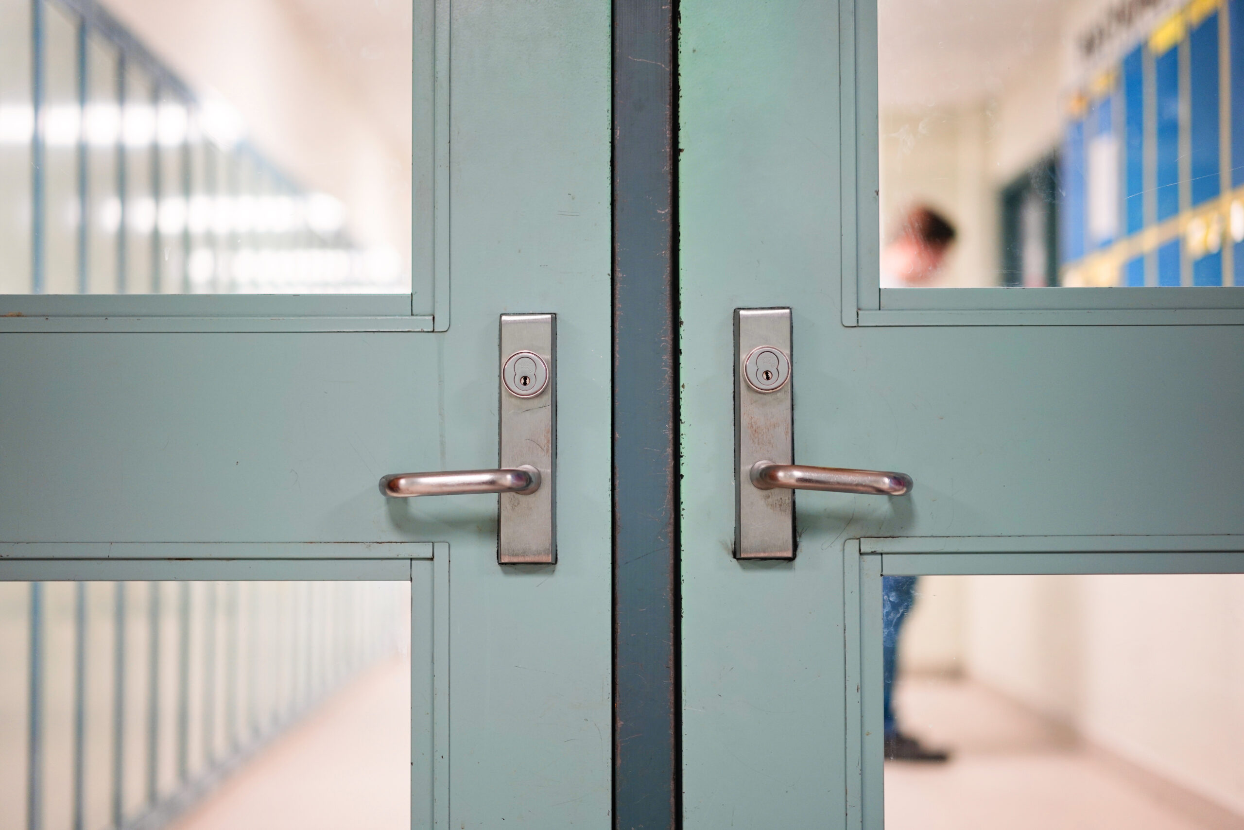 A set of locked doors with a school hallway beyond.