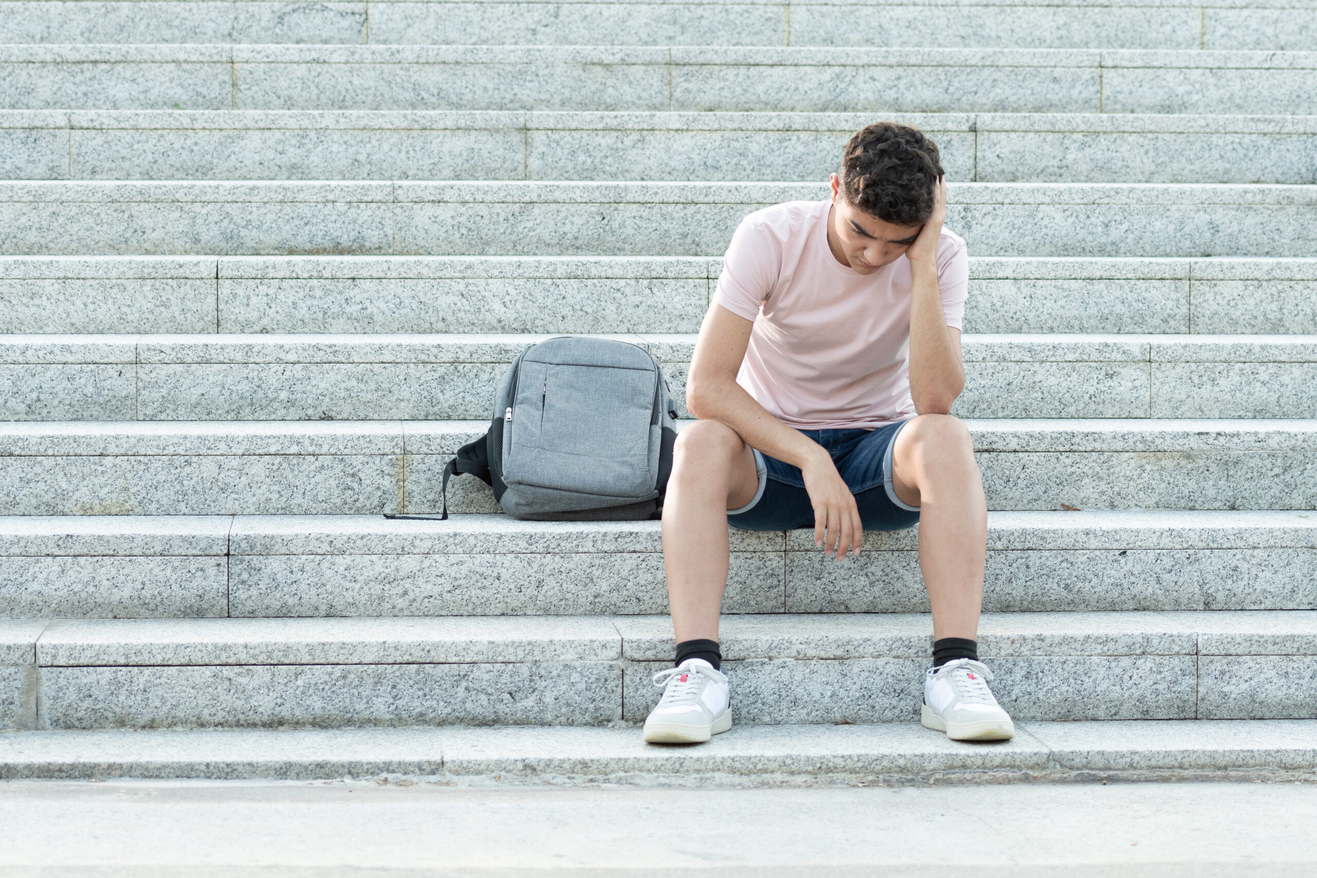 Junge mit Rucksack sitzt auf Stufen, Kopf in Handfläche