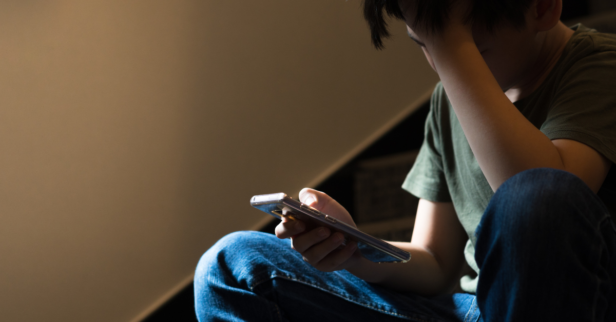 young boy looking at his phone in one hand and his head in the other, upset by what's happening on the screen