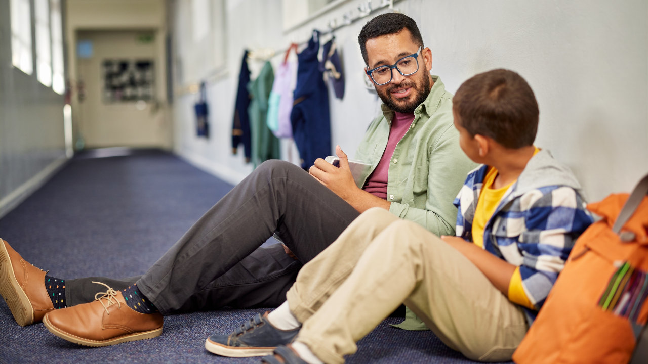 A trust adult sits with a student discussing something in a hallway