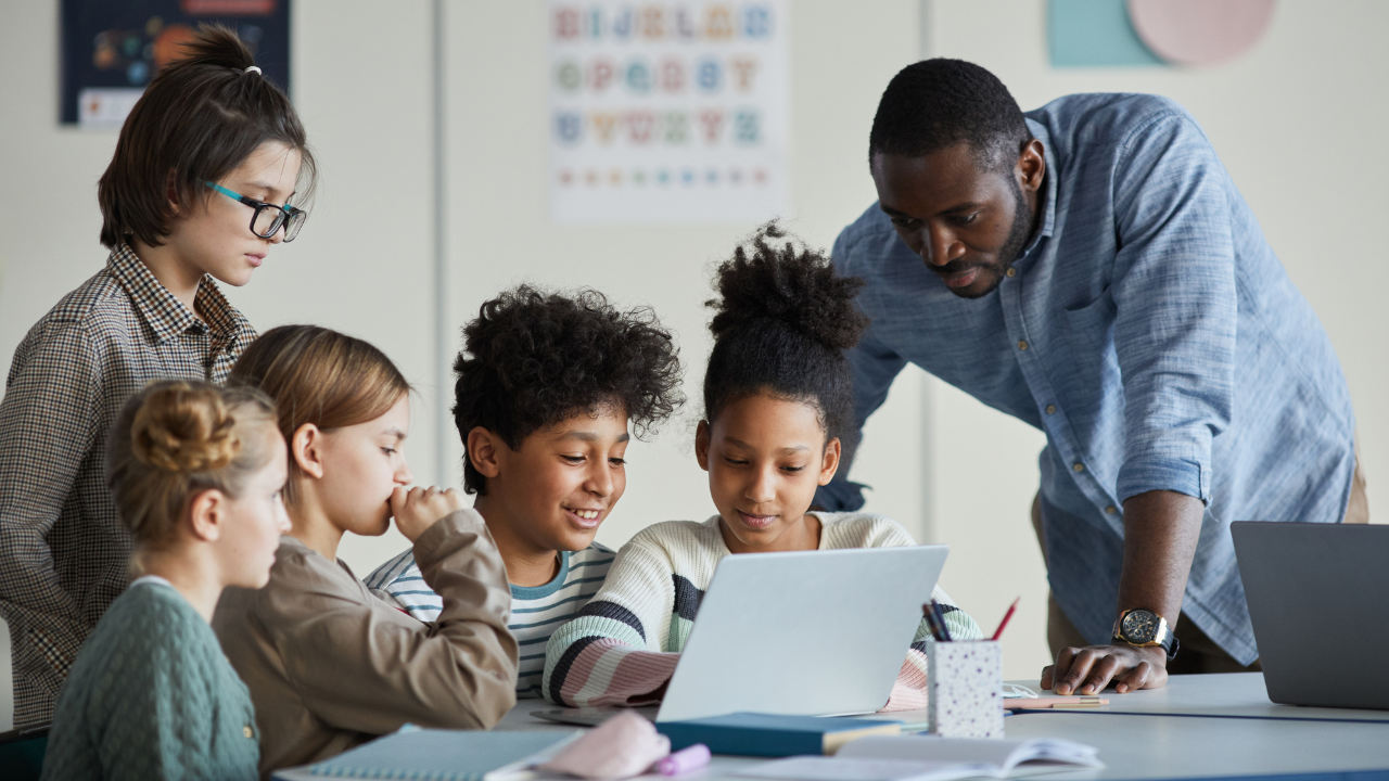 teachers lending a hand to a group of children working on a tablet